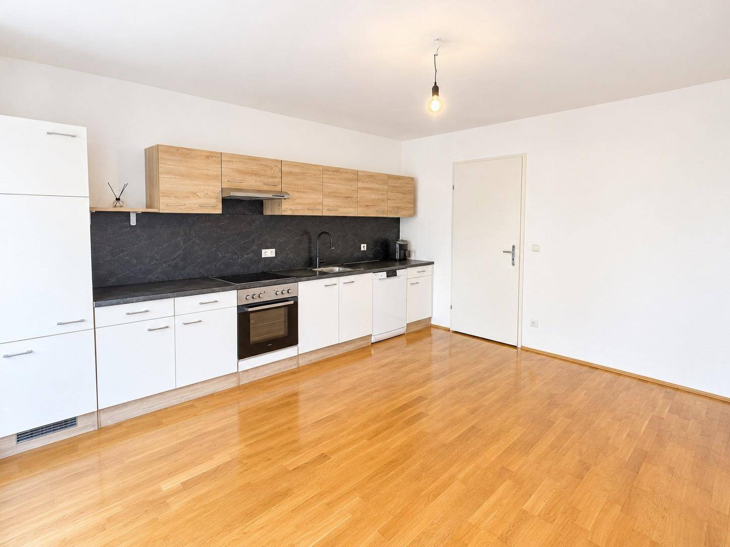 Geräumiger Wohnbereich mit integrierter Küche, Parkettboden und weiß gestrichenen Wänden.