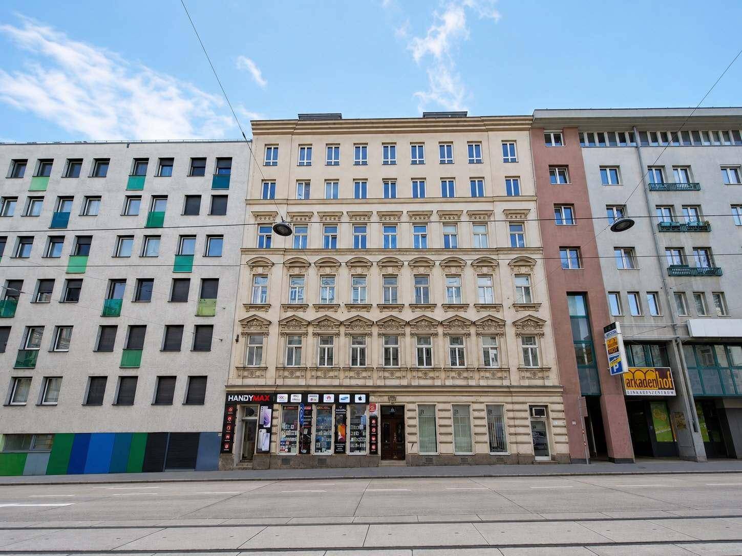 Historisches Gebäude mit reich verzierter Fassade und Geschäften im Erdgeschoss an einer Stadtstraße.