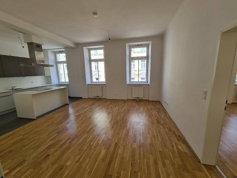 Heller offener Wohnbereich mit Holzboden und integrierter Küchenzeile, bereit zur Einrichtung.