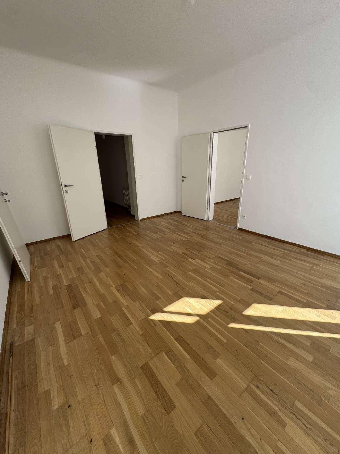 Helles Zimmer mit Parkettboden und mehreren Türen, die zu anderen Räumen führen, gut gepflegt.