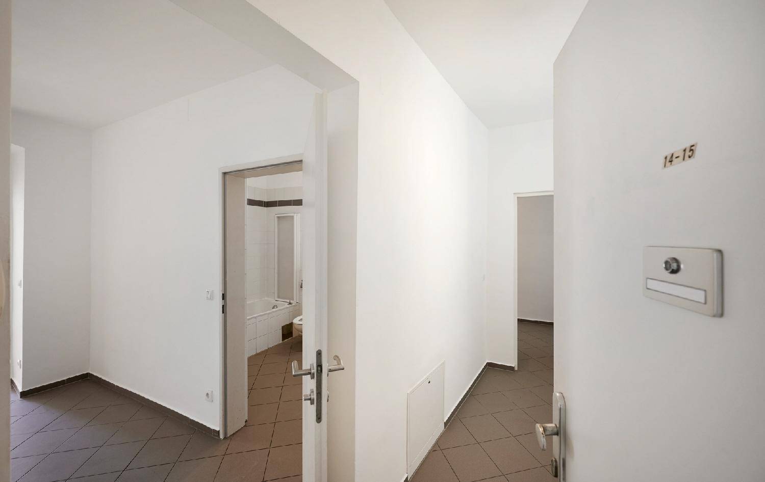 Heller Flur mit grauen Fliesenboden und Zugang zu verschiedenen Räumen der Wohnung.