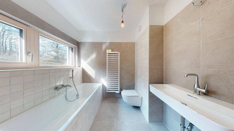 Modernes Badezimmer mit Badewanne, Wand-WC, Einzelwaschbecken und beheiztem Handtuchhalter.
