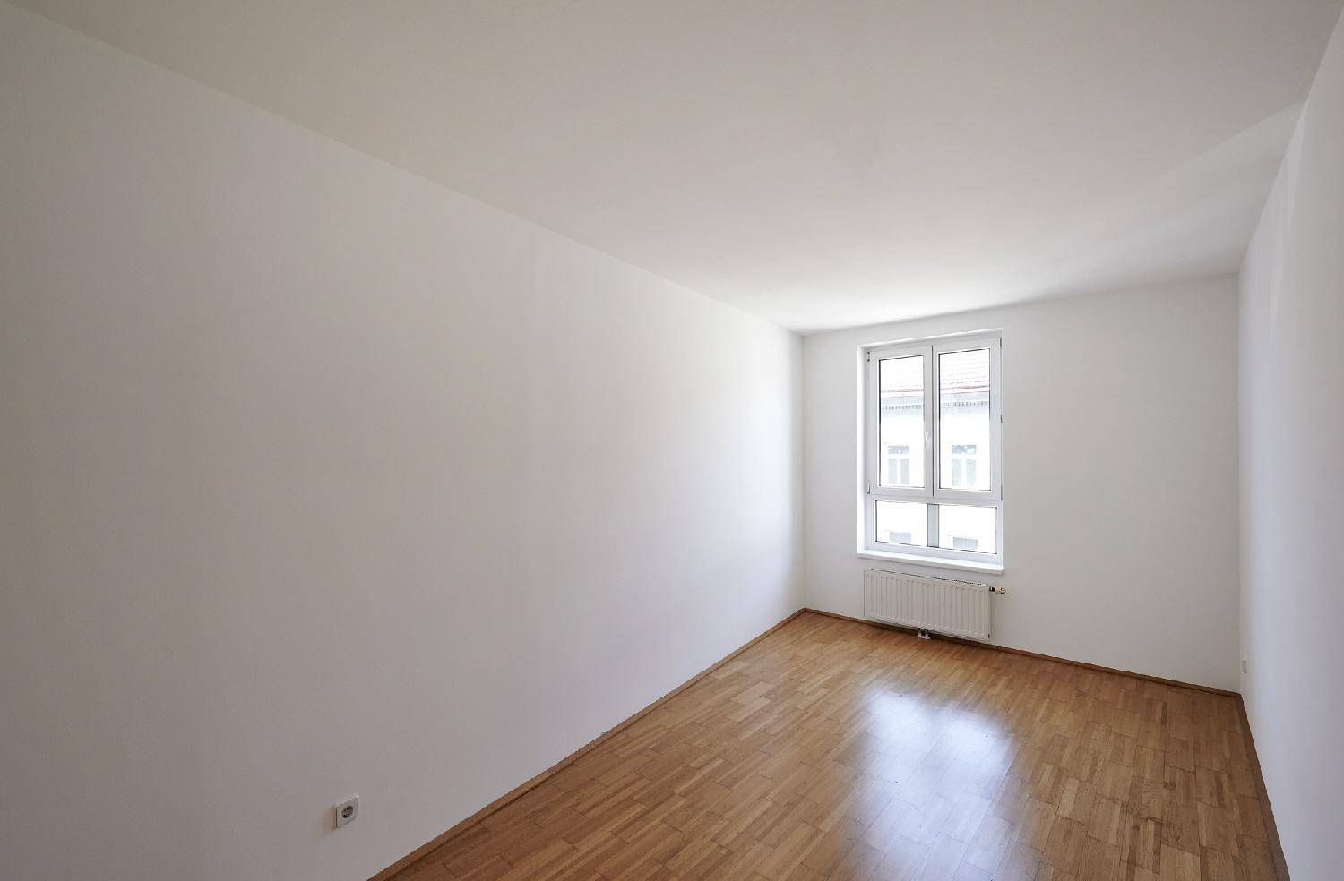 Ruhiges Zimmer mit Holzboden und einem Fenster, das viel natürliches Licht hereinlässt.