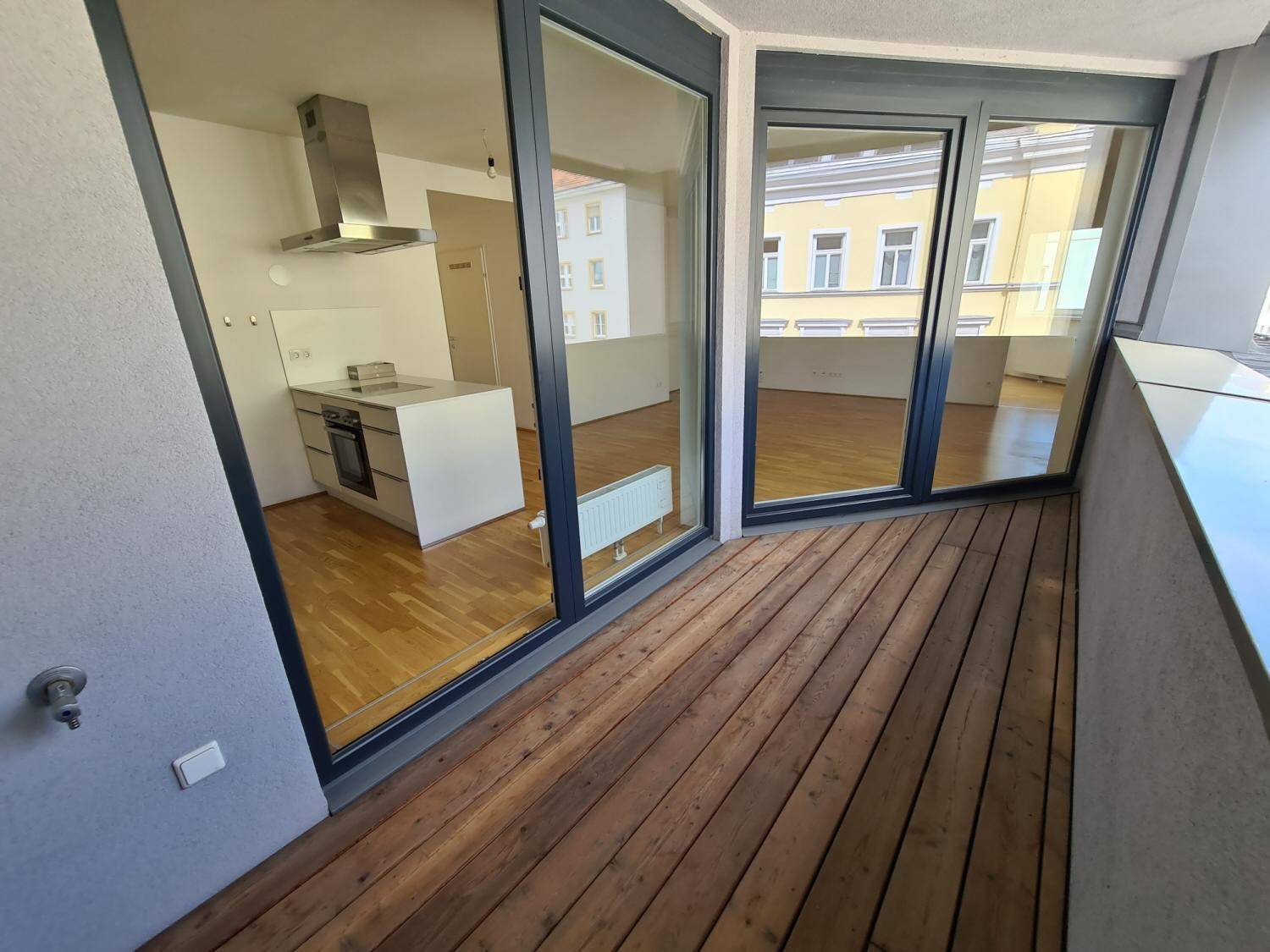 Balkon mit Holzboden und Blick in den offenen Wohnbereich mit Küche.