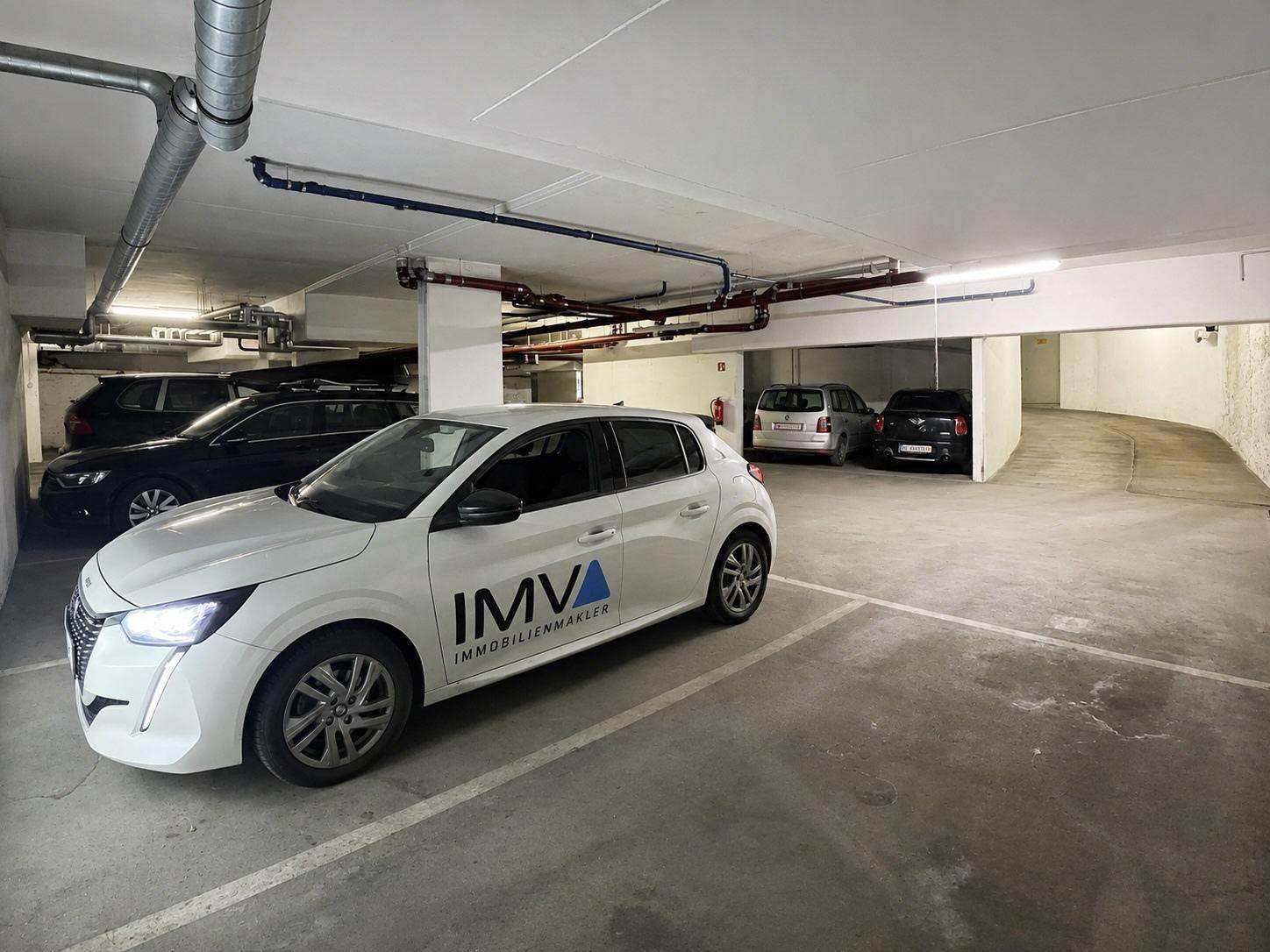 Tiefgarage mit mehreren Stellplätzen und einem Immobilienmaklerfahrzeug.