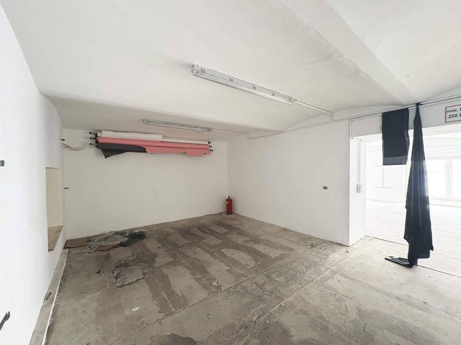 Kleinerer Bereich des Gewerberaums mit Betonboden, Feuerlöscher und weißen Wänden, bereit zur Gestaltung.