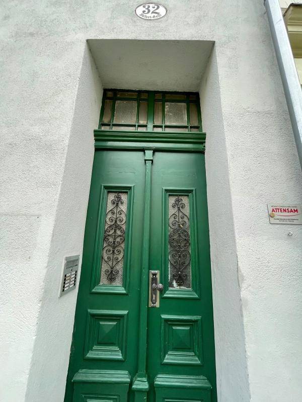 Grüne Eingangstür mit dekorativen Gittern und Hausnummer 32 an einer weißen Fassade.