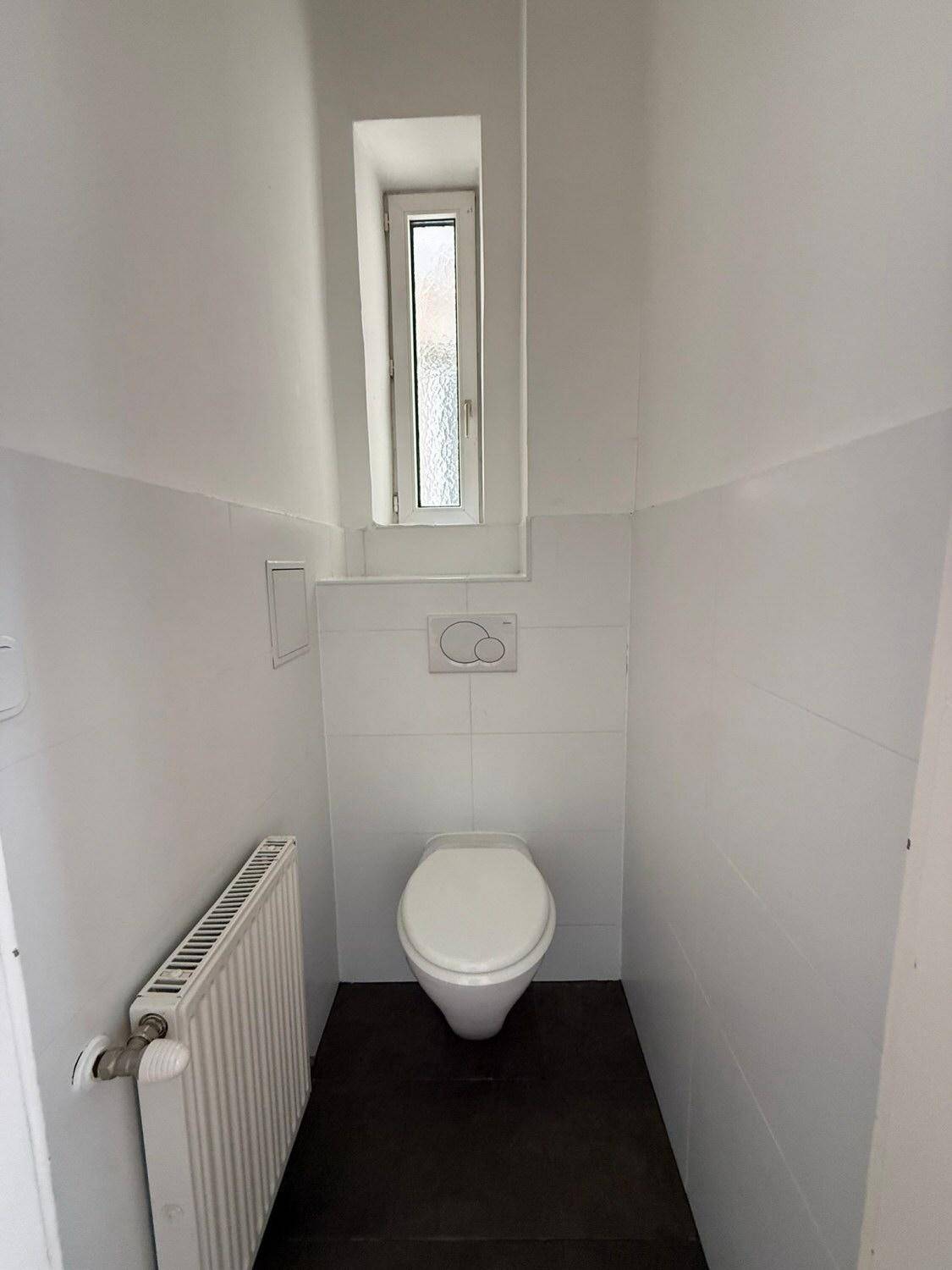 Kleines separates WC mit Wand-WC, weißen Fliesen und einem schmalen Fenster.