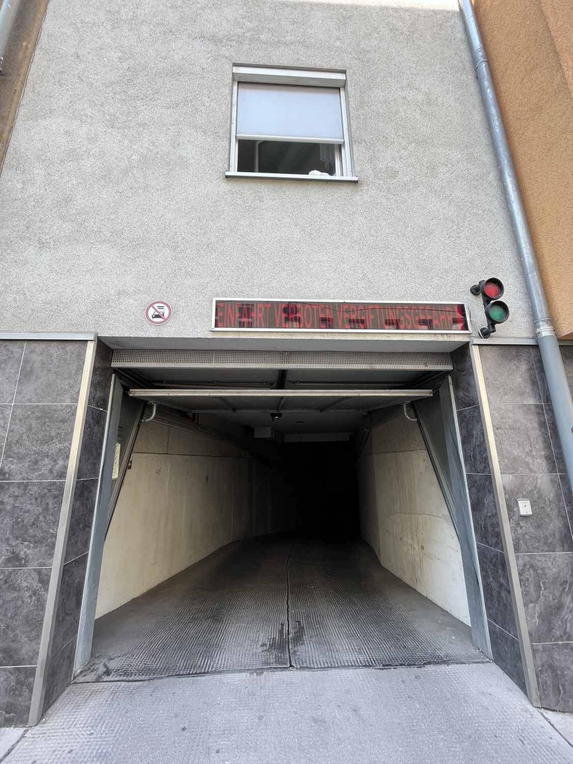 Eingang zur Tiefgarage von der Straße aus, mit Ampel und Hinweisschild über der Einfahrt.