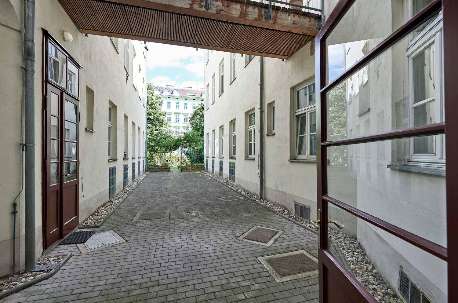 Gepflasterter Innenhof zwischen Gebäuden mit Zugang zu den Eingängen und Blick auf den Himmel.