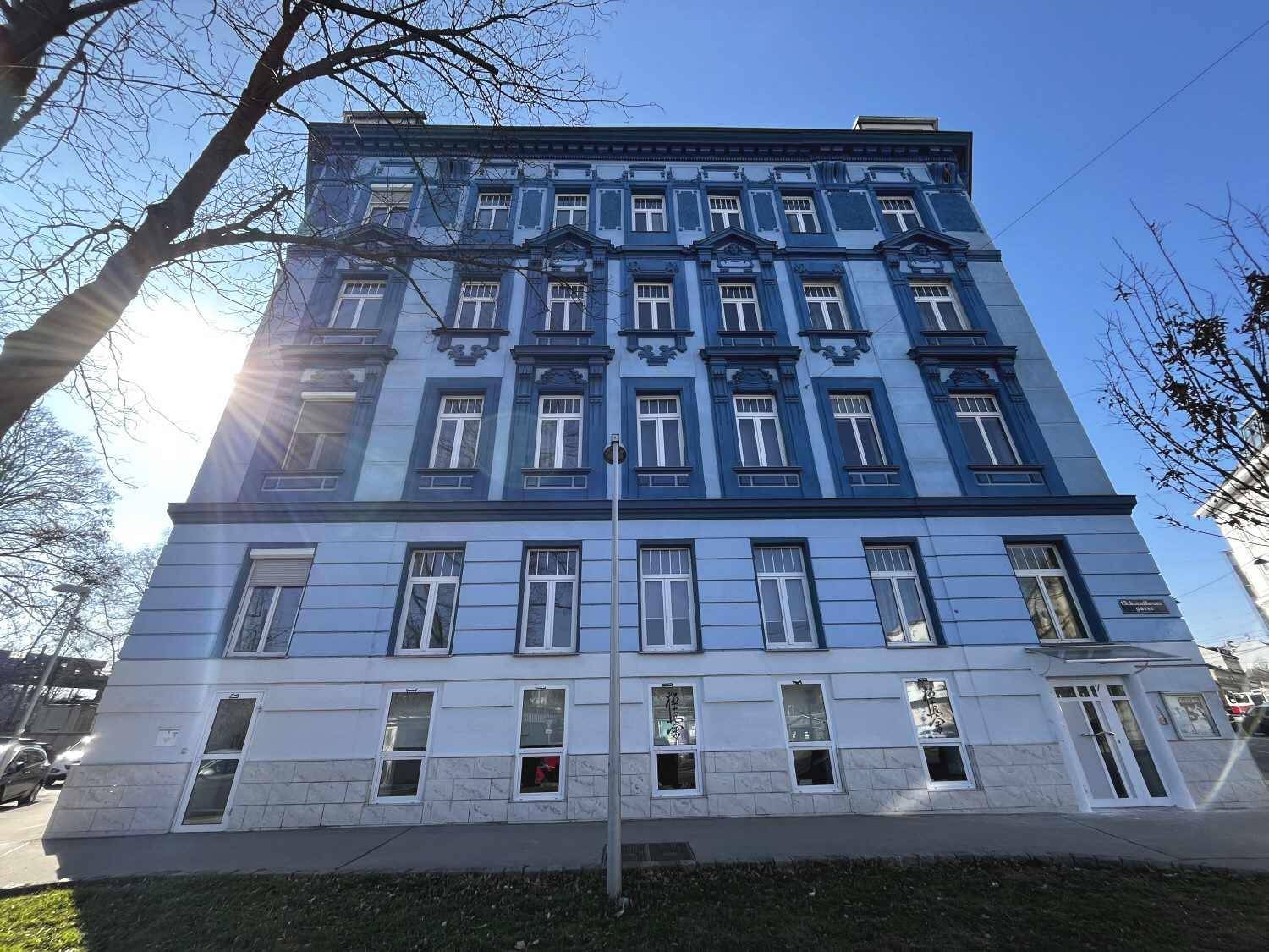Detailansicht der blauen Fassade eines Altbaus mit vielen Fenstern im Sonnenlicht.