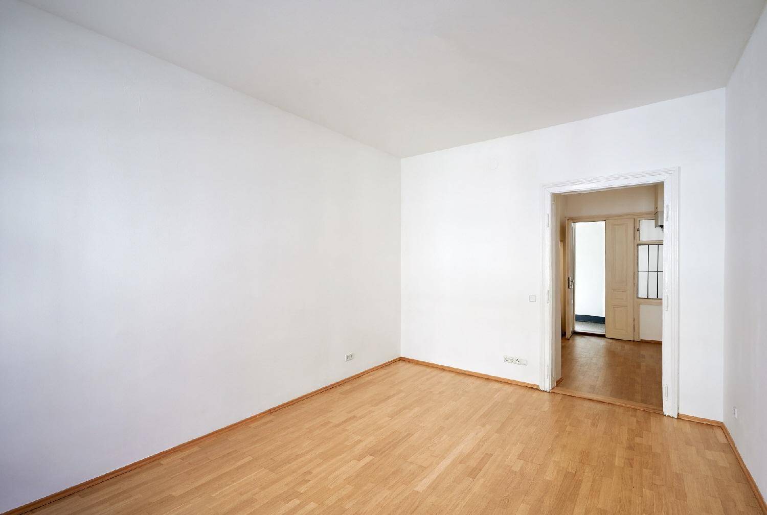 Geräumiger, heller Raum mit Parkettboden und offenem Durchgang zu einem weiteren Zimmer.