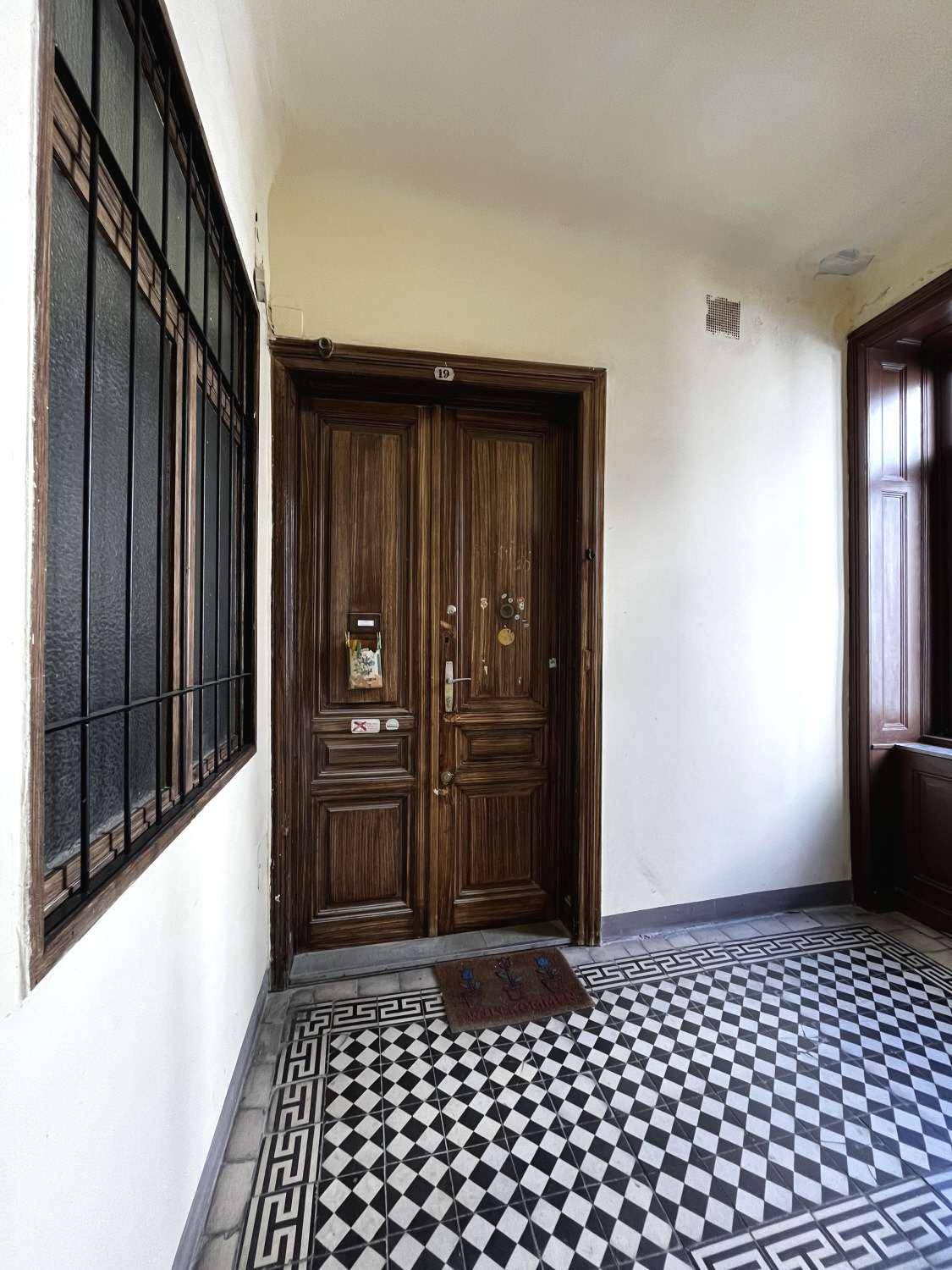 Eingangsbereich mit einer verzierten Holztür, Gitterfenster und einem schwarz-weiß gemusterten Fliesenboden.