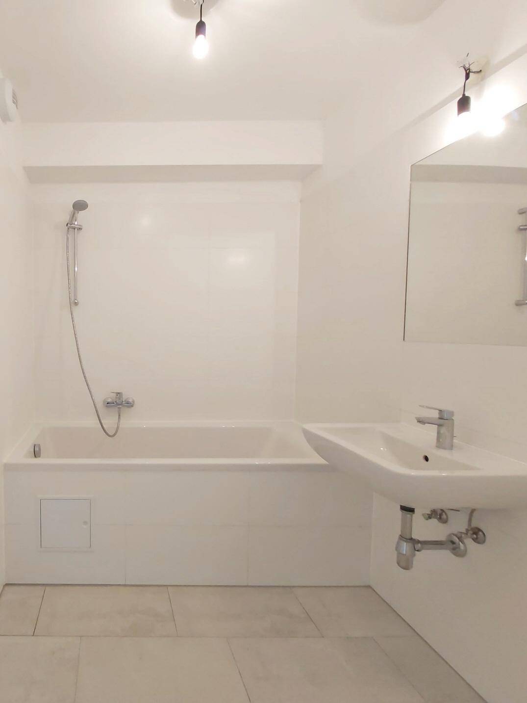 Modernes Badezimmer mit Badewanne, Waschbecken und Spiegel, in hellen Farbtönen gehalten.