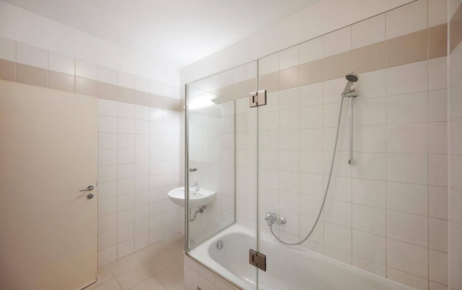 Helles Badezimmer mit Badewanne, Duschvorrichtung und weiß gefliesten Wänden.
