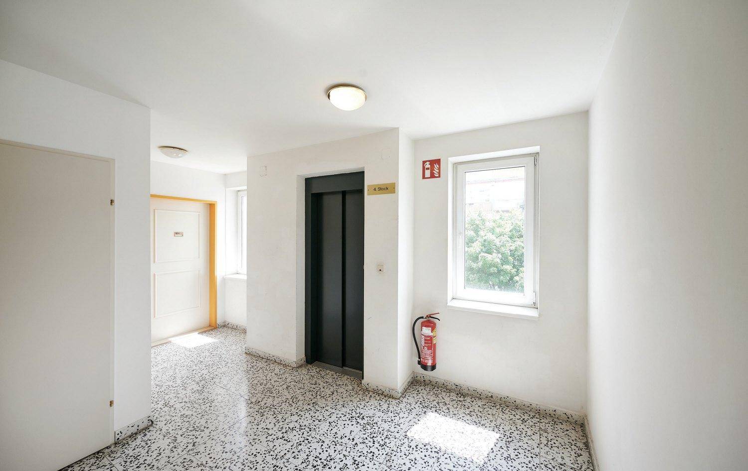 Gemeinschaftlicher Flur mit Aufzug, Fenster und Terrazzoboden.