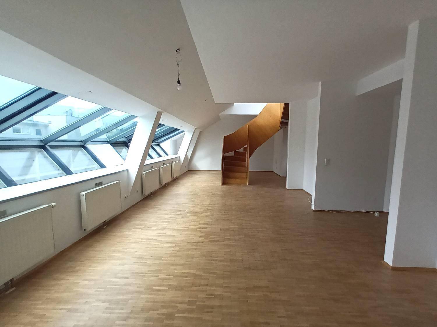 Heller Dachgeschossraum mit großen Dachfenstern, Holzparkettboden und einer modernen Holztreppe.