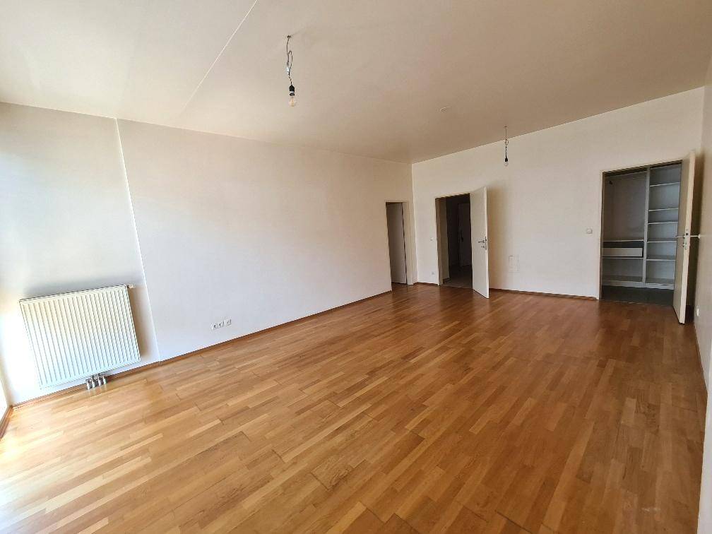 Geräumiges Wohnzimmer mit Parkettboden und Zugang zu weiteren Räumen und Stauraum.