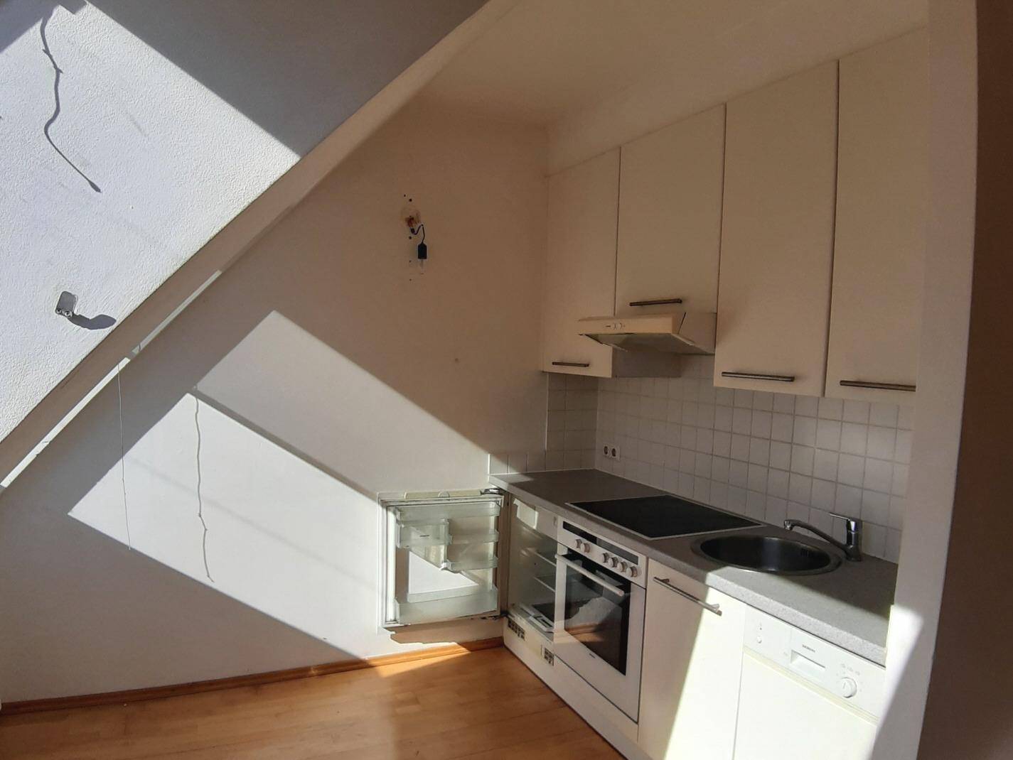 Helle Küchenzeile in einem Dachgeschosszimmer mit weißen Schränken und integrierten Geräten.