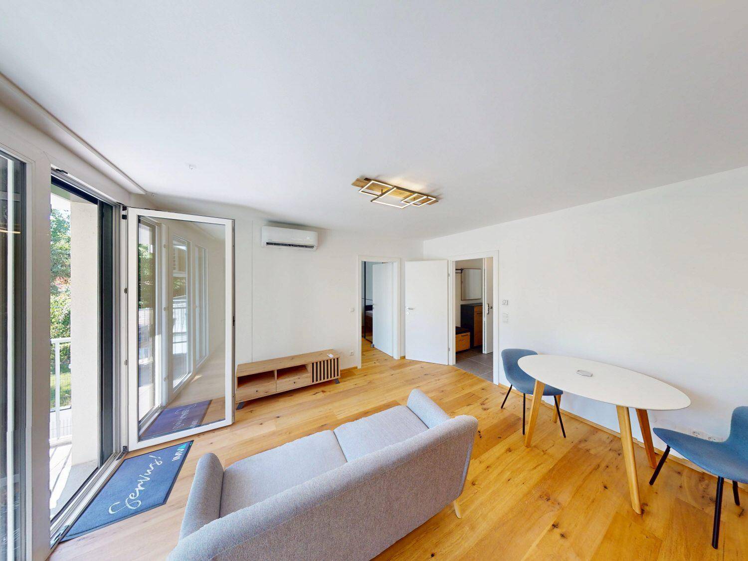 Geräumiges Wohnzimmer mit Holzboden, moderner Einrichtung und großen Fenstern zum Balkon.