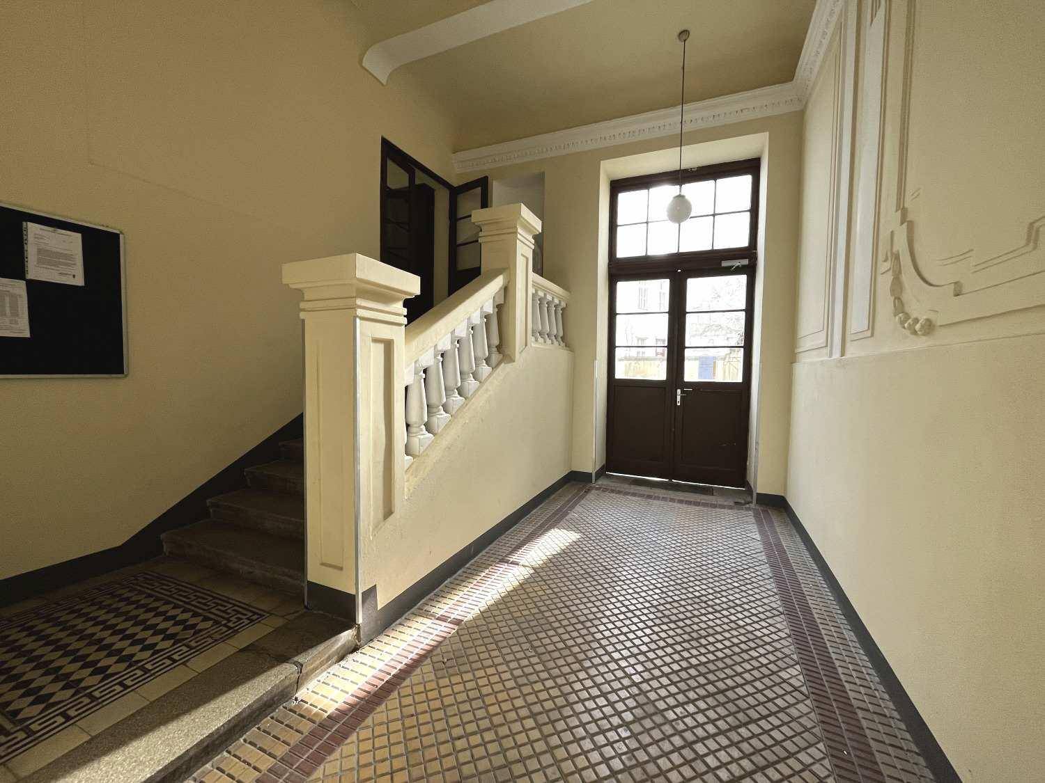 Eingangsbereich eines Altbaus mit gemustertem Fliesenboden, Treppe und hohen Decken.