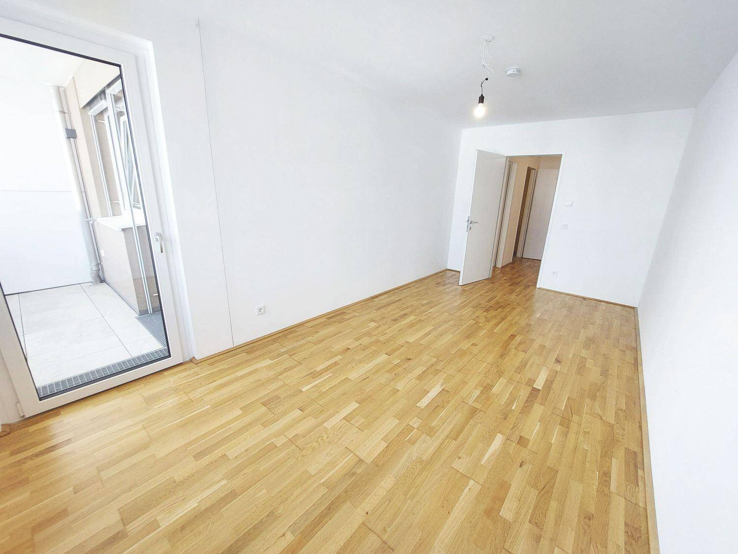 Heller Raum mit Parkettboden und direktem Zugang zu einem Balkon.