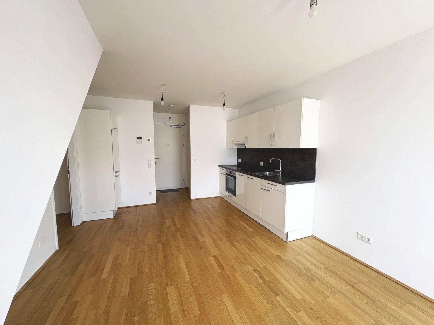 Offener Wohnbereich mit Holzboden, weißer Küchenzeile und Zugang zum Eingangsbereich.