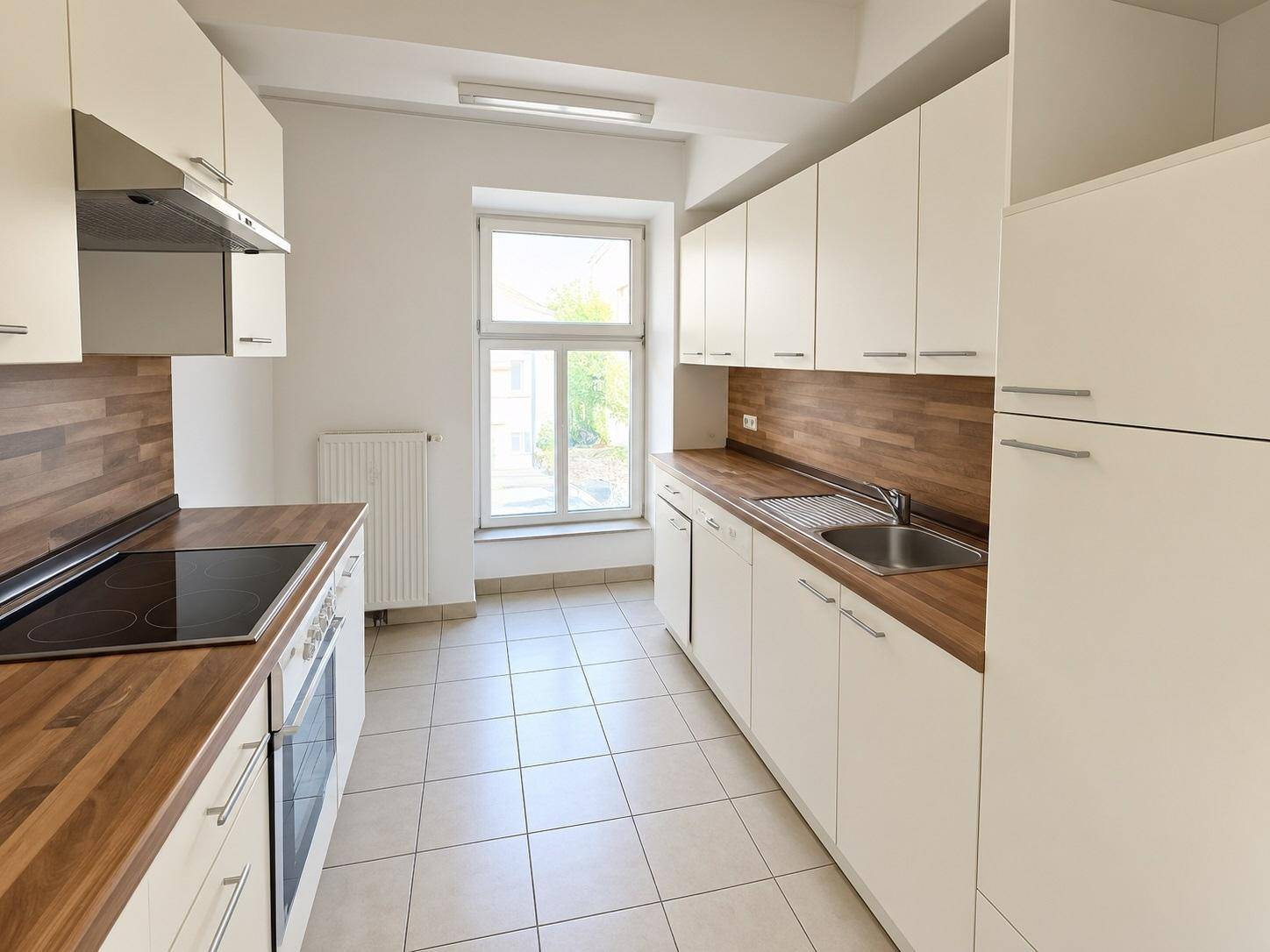 Moderne Einbauküche mit weißen Schränken, Holz-Arbeitsplatten und Fliesenboden, inklusive Herd und Spüle.
