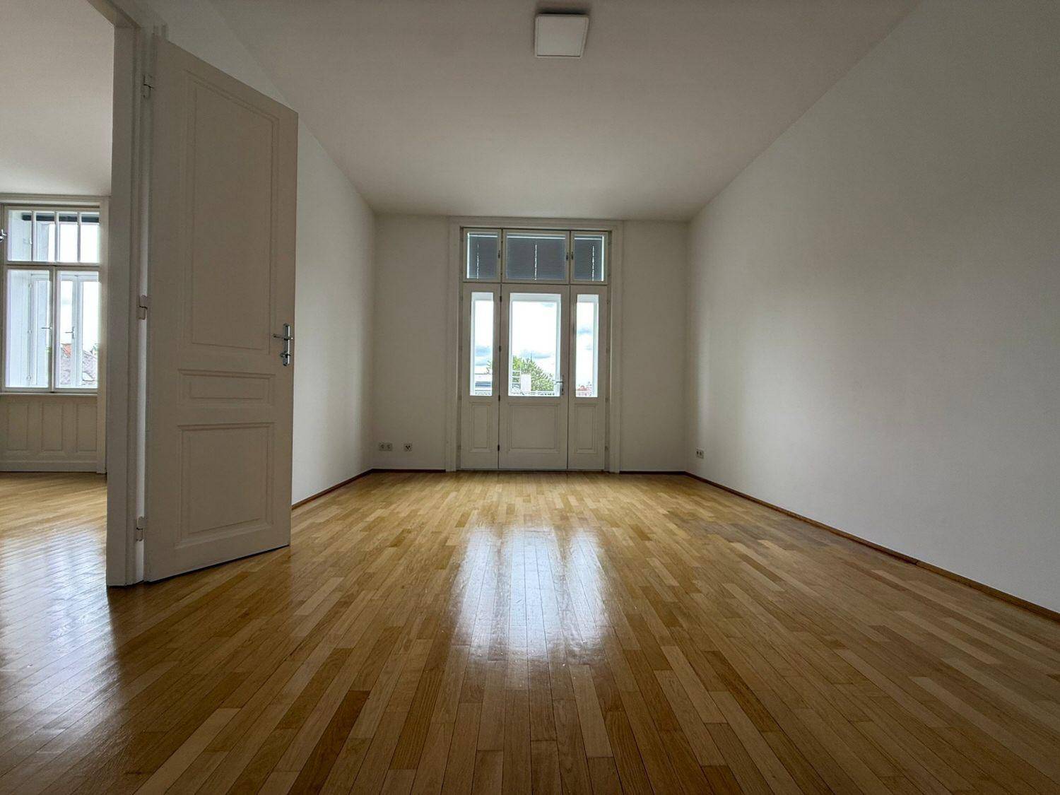 Heller Raum mit Parkettboden und großer Glastür, die Zugang zu einem Außenbereich bietet.