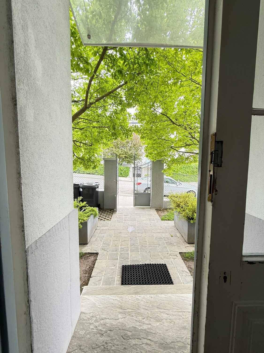 Blick vom Eingangsbereich durch die offene Tür auf den begrünten Vorgarten.