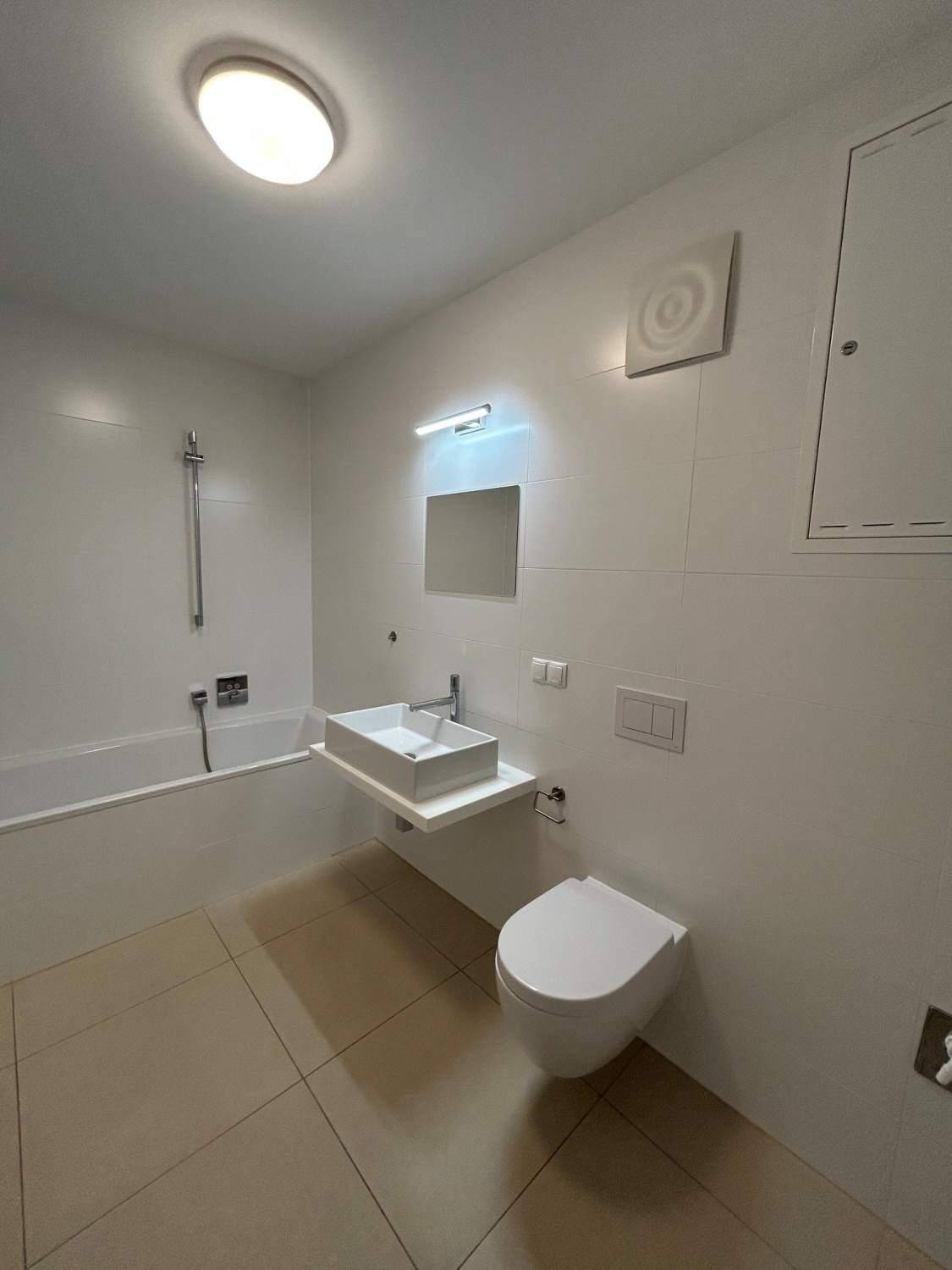 Modernes Badezimmer mit weißen Fliesen, Badewanne, Hänge-WC und Waschbecken.