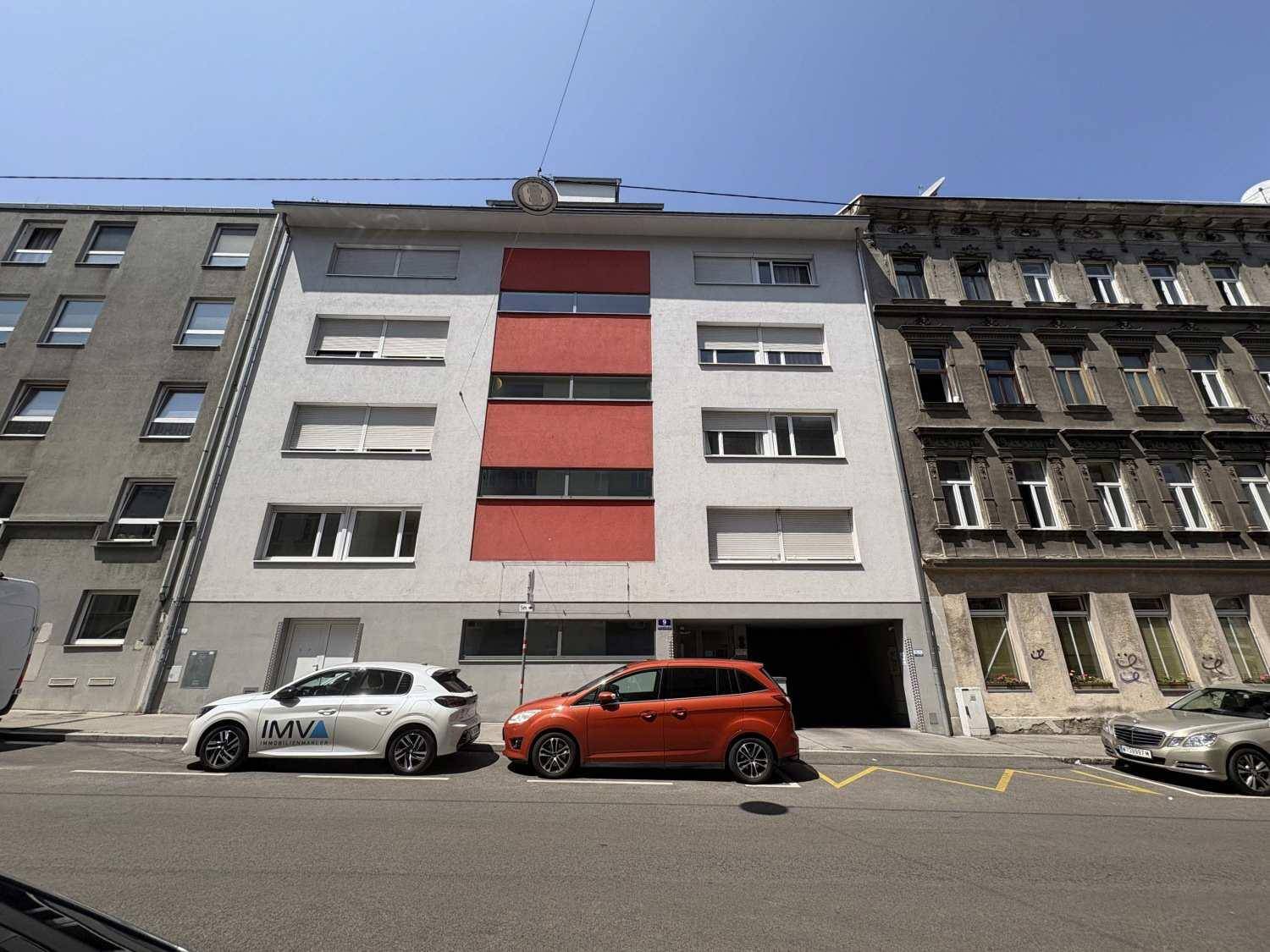 Moderne Wohnhausfassade mit roten Akzenten und großen Fenstern an einer Stadtstraße.