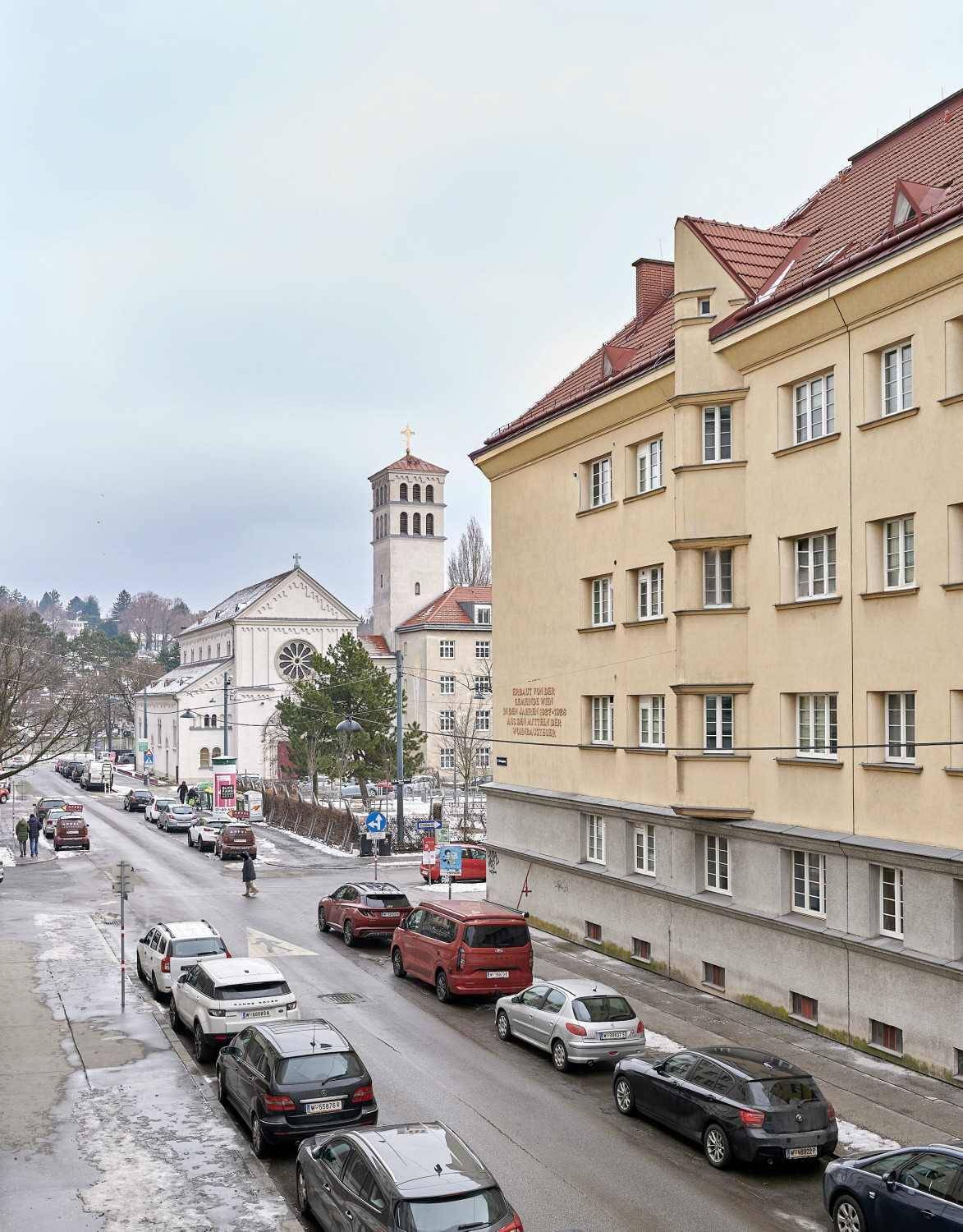 Stadtansicht mit einer Kirche im Hintergrund, einer belebten Straße und parkenden Autos.