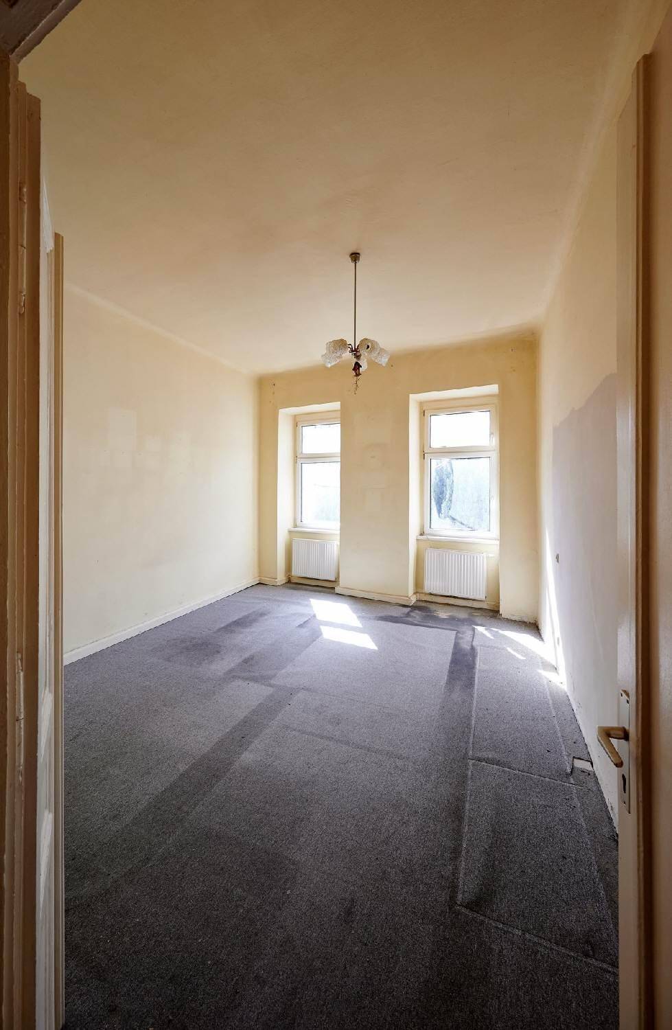 Leerer Raum mit Teppichboden und zwei Fenstern, bereit für eine Renovierung.