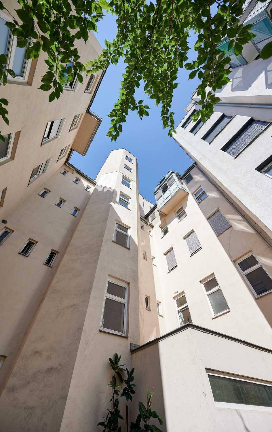 Blick in den Innenhof eines Gebäudes mit vielen Fenstern und etwas Grün.