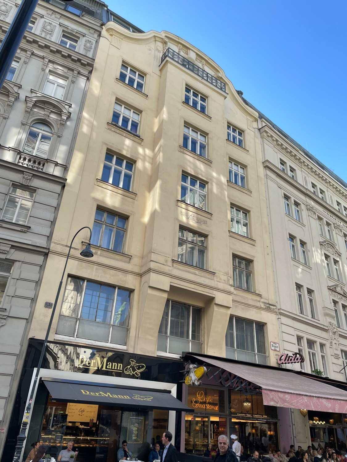 Historische Fassade eines Gebäudes mit Geschäften im Erdgeschoss und eleganten Fenstern in den oberen Etagen.