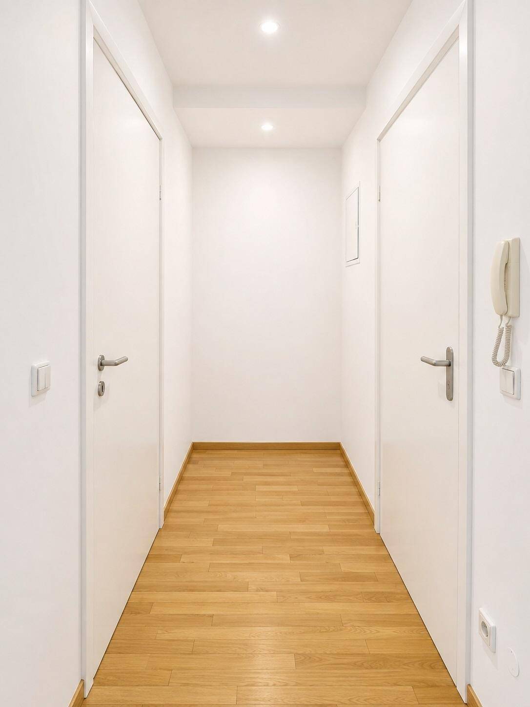 Heller Flur mit Holzboden und weißen Türen, der verschiedene Räume miteinander verbindet.
