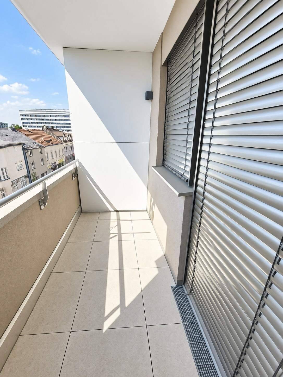 Schmaler, sonniger Balkon mit Fliesenboden und Jalousien am Fenster, ideal zum Entspannen.