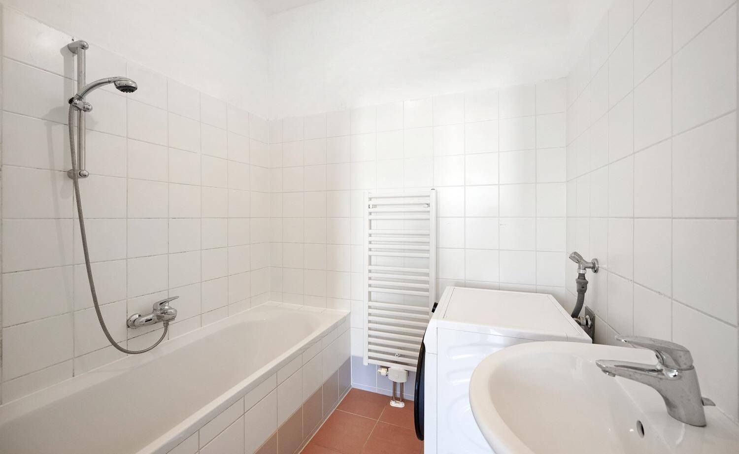 Gefliestes Badezimmer mit Badewanne, Duschfunktion, Waschmaschinenanschluss und Handtuchheizkörper.