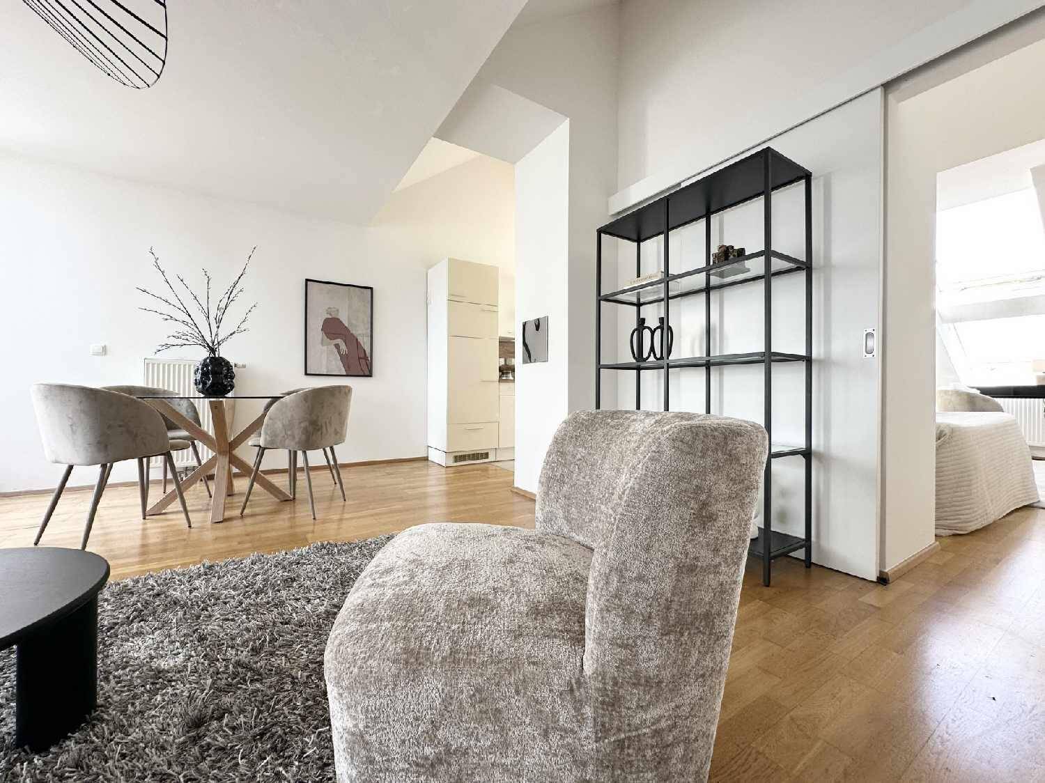Offener Wohn-Essbereich mit Holzboden, modernem Regal und Blick in das angrenzende Schlafzimmer.