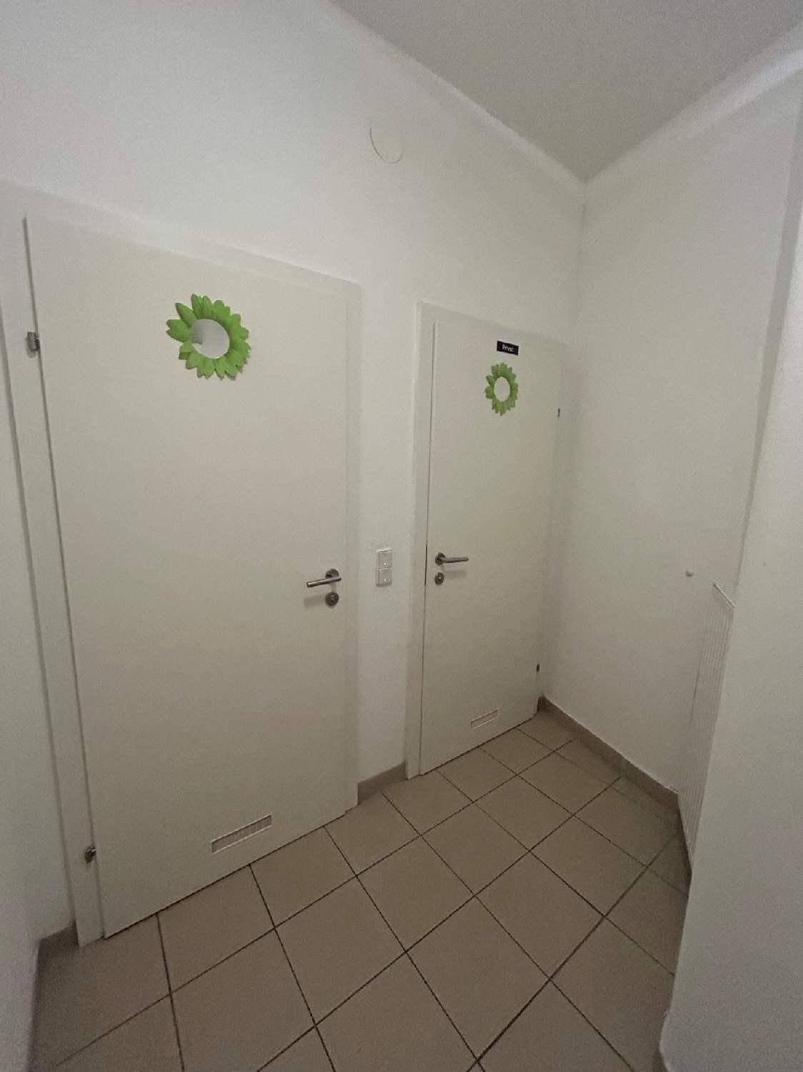 Zwei weiße Türen in einem Flur, wahrscheinlich zu Toiletten führend, mit kleinen grünen Dekorationen.