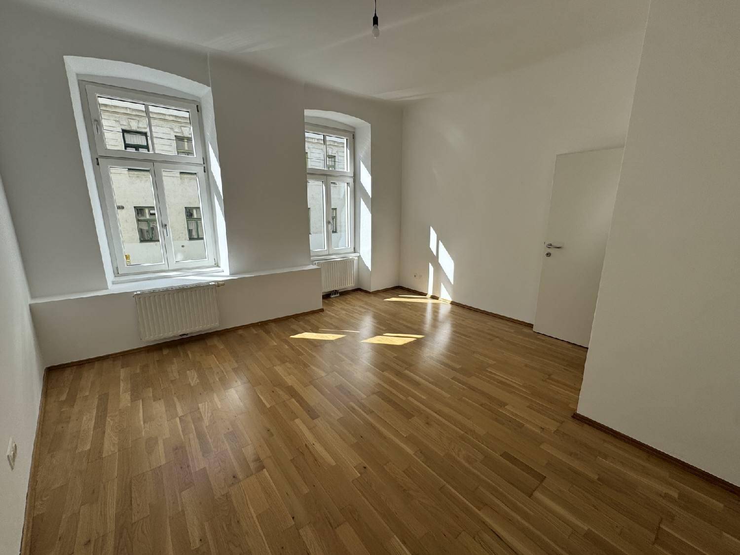 Geräumiges, helles Zimmer mit Parkettboden und zwei Fenstern, das viel Tageslicht empfängt.