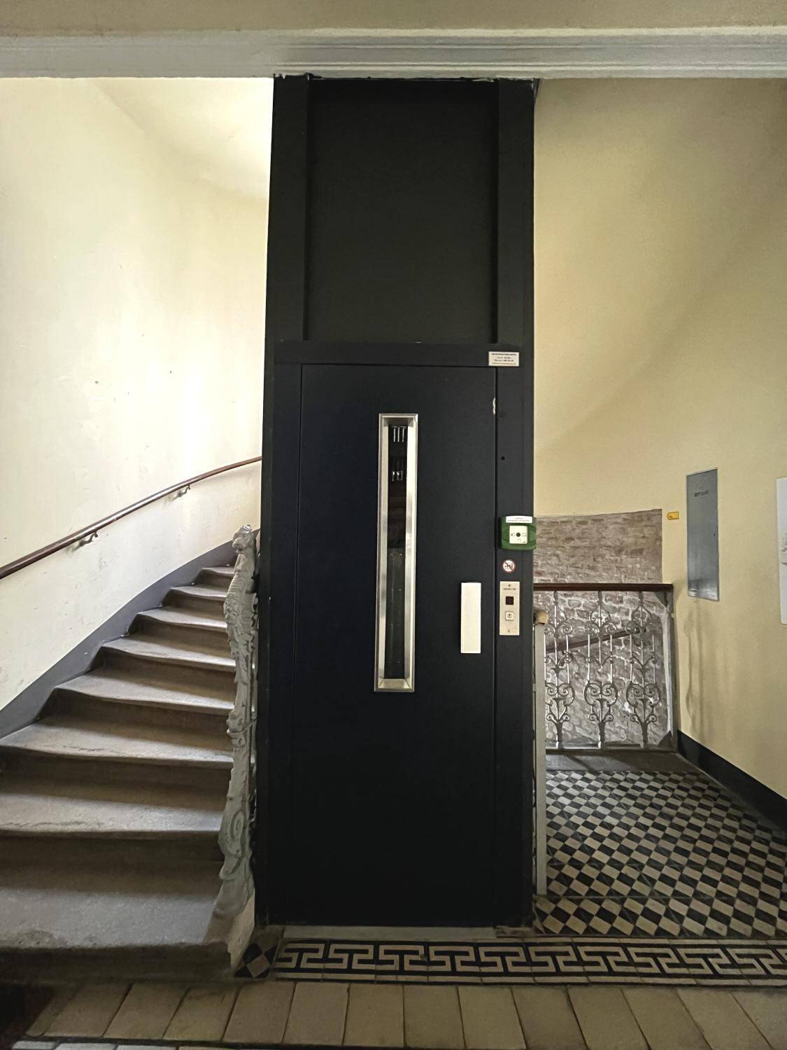 Treppenhaus eines Altbaus mit modernem Aufzug und traditionellem Fliesenboden.