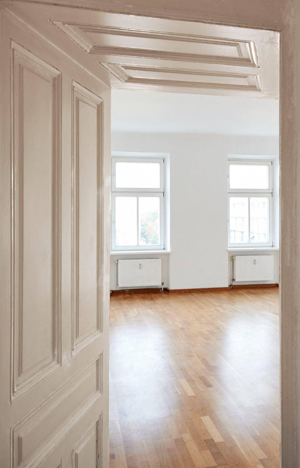 Blick durch eine klassische, offene Tür in ein helles Zimmer mit glänzendem Parkettboden.