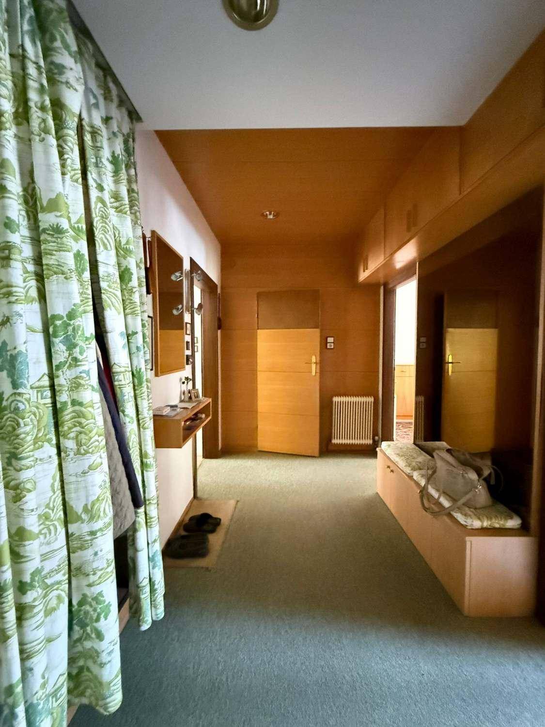 Langer Flur mit Holzvertäfelung an Wänden und Decke, grünem Teppichboden und einer Sitzbank.