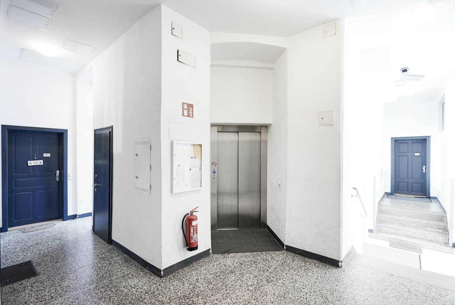 Heller Flur mit Aufzug und Terrazzoboden in einem Mehrfamilienhaus.