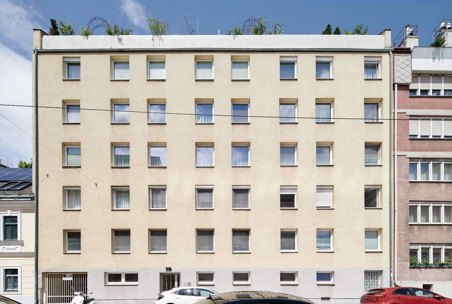 Fassade eines Mehrfamilienhauses mit vielen Fenstern unter blauem Himmel.