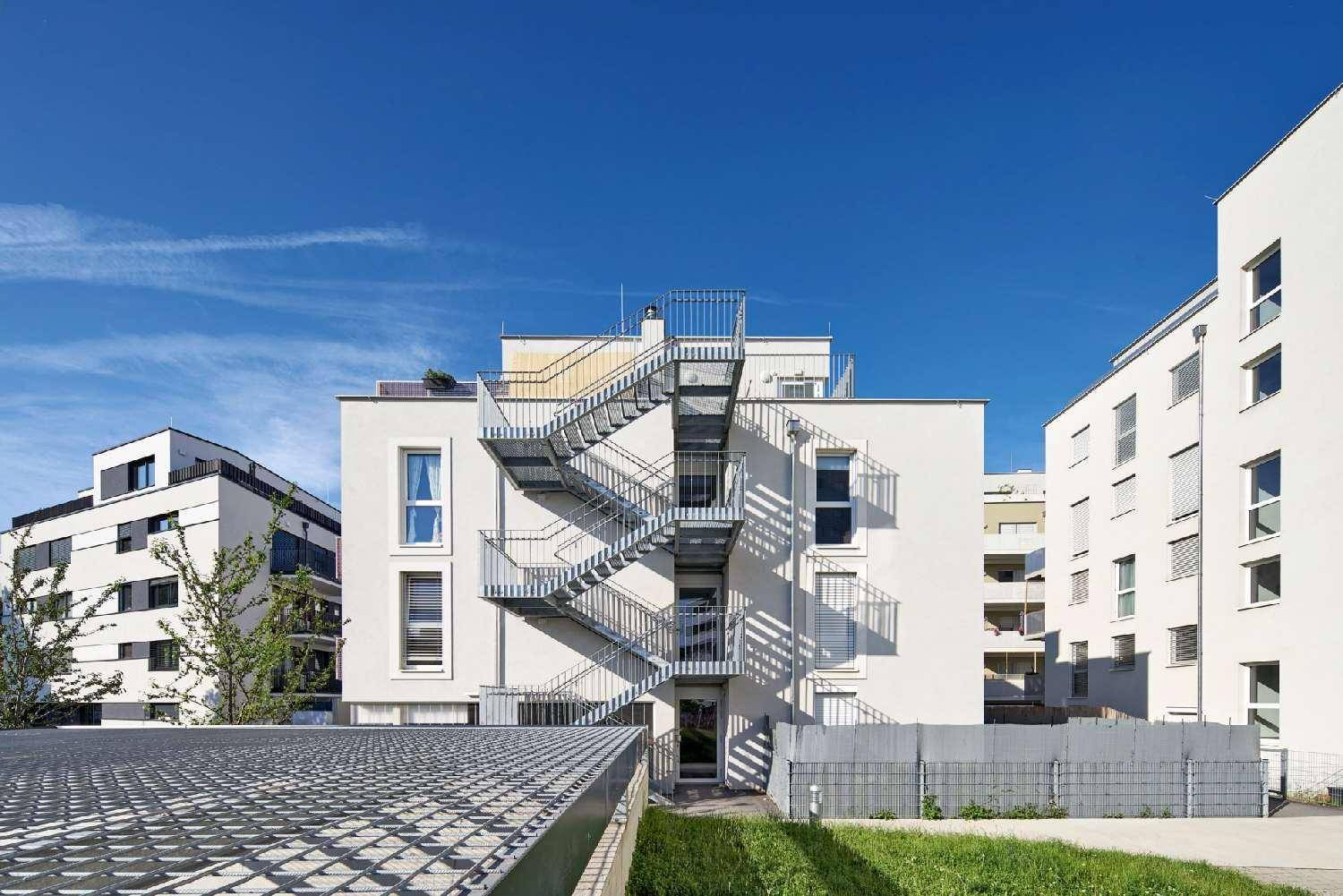 Moderne Gebäudefassade mit externer Metalltreppe unter strahlend blauem Himmel und Sonnenschein.