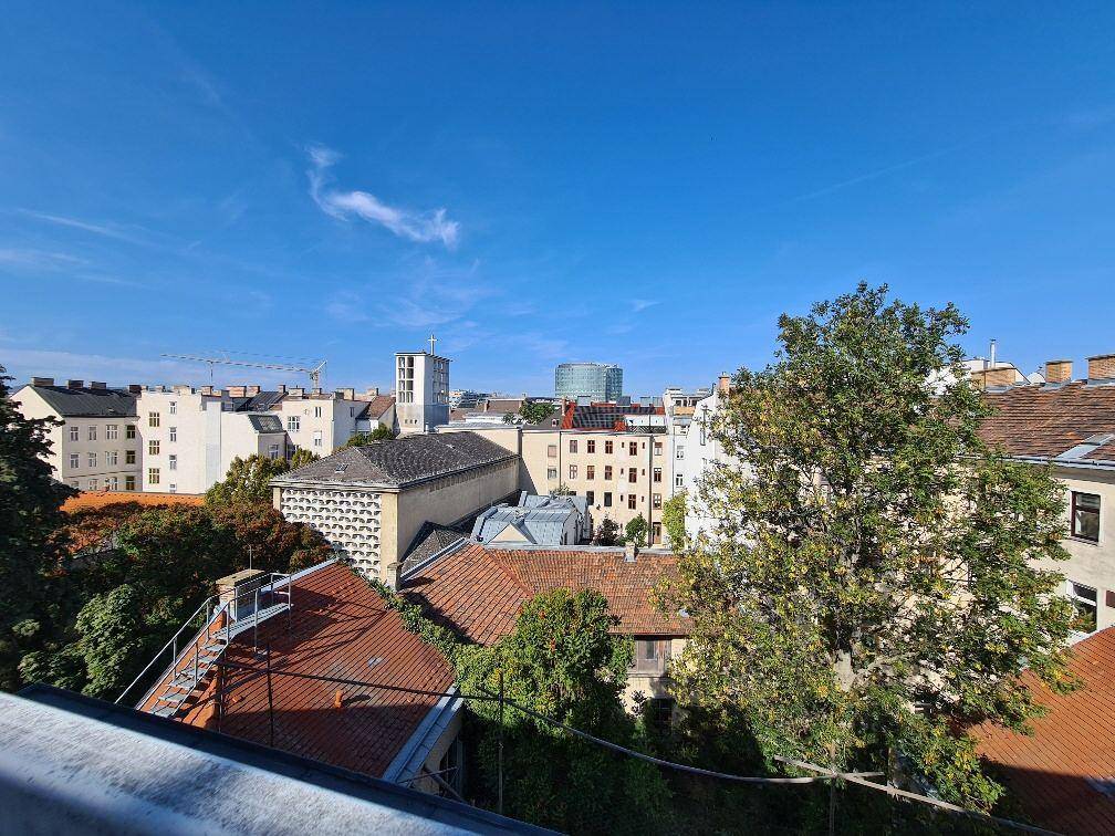 Weitblick über die Dächer der Stadt mit Bäumen und einem klaren blauen Himmel.