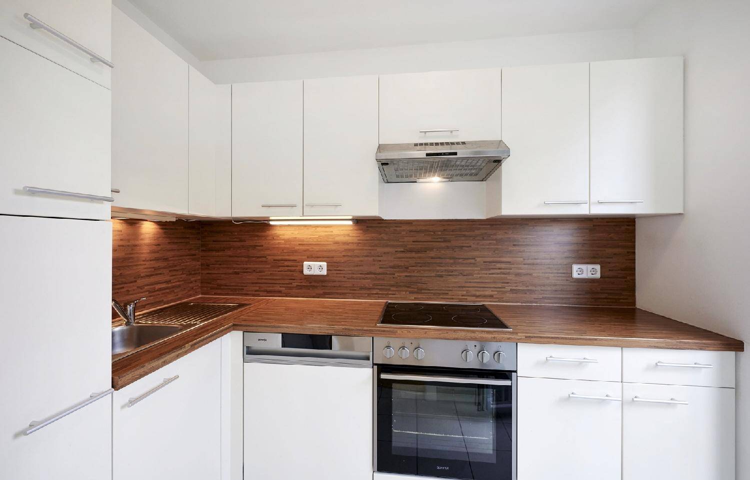 Moderne Einbauküche mit weißen Schränken, Holz-Arbeitsplatten und integrierten Elektrogeräten.